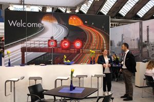 Der Stand des Meiser Straßenbau mit Mitarbeitenden bei der Messe Intertraffic in Amsterdam, mit einem großen Plakat von einer Autobahn mit Leitplanken.